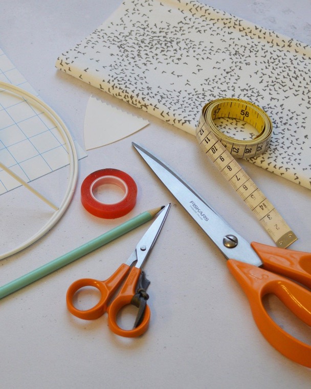 Everything for the workshop laid out: printed fabric, a tape measure, scissors, tape, a pencil and the lampshade rings