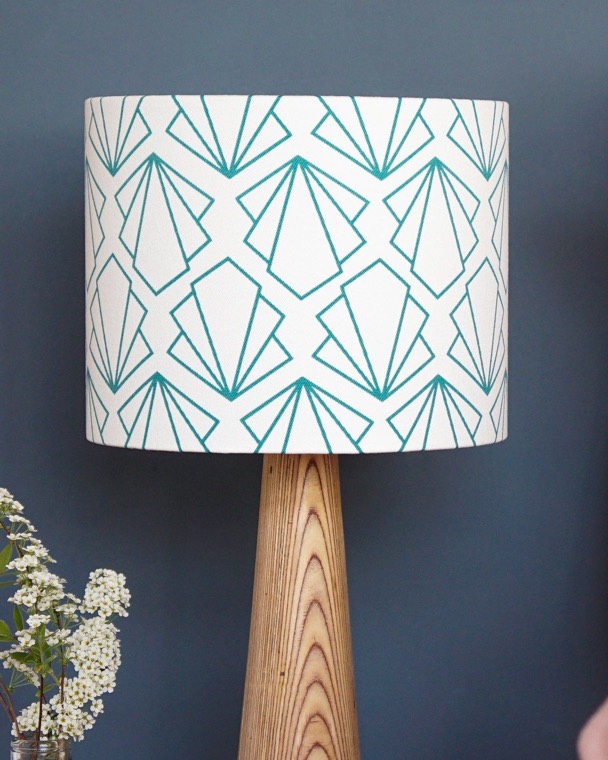A finished drum lampshade in a turquoise geometric print, on a wooden lamp base