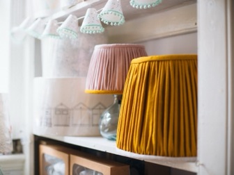 Pleated pink and mustard shades on a shelf in the Lume studio, with a string of tiny shades above